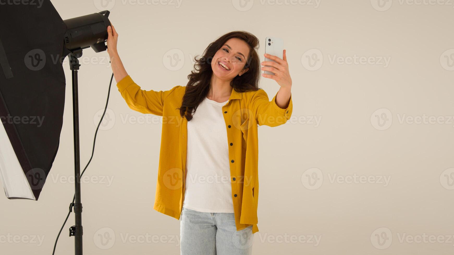 Smiling cheerful Caucasian woman female influencer blogger shooting blog wave hello mobile phone smartphone. Girl vlogger talk walk showing studio clothes streaming broadcast live online at home photo