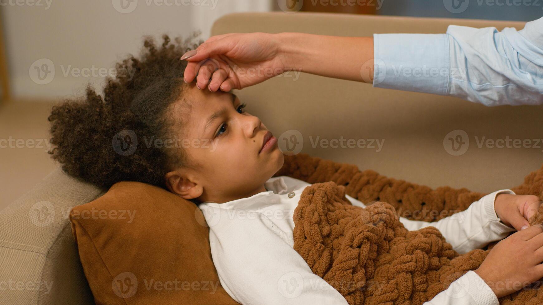 Mother hands cover African American daughter blanket cough temperature touching forehead ill flu heat fever unhealthy influenza pandemic virus childcare parent child kid little girl respiratory home photo