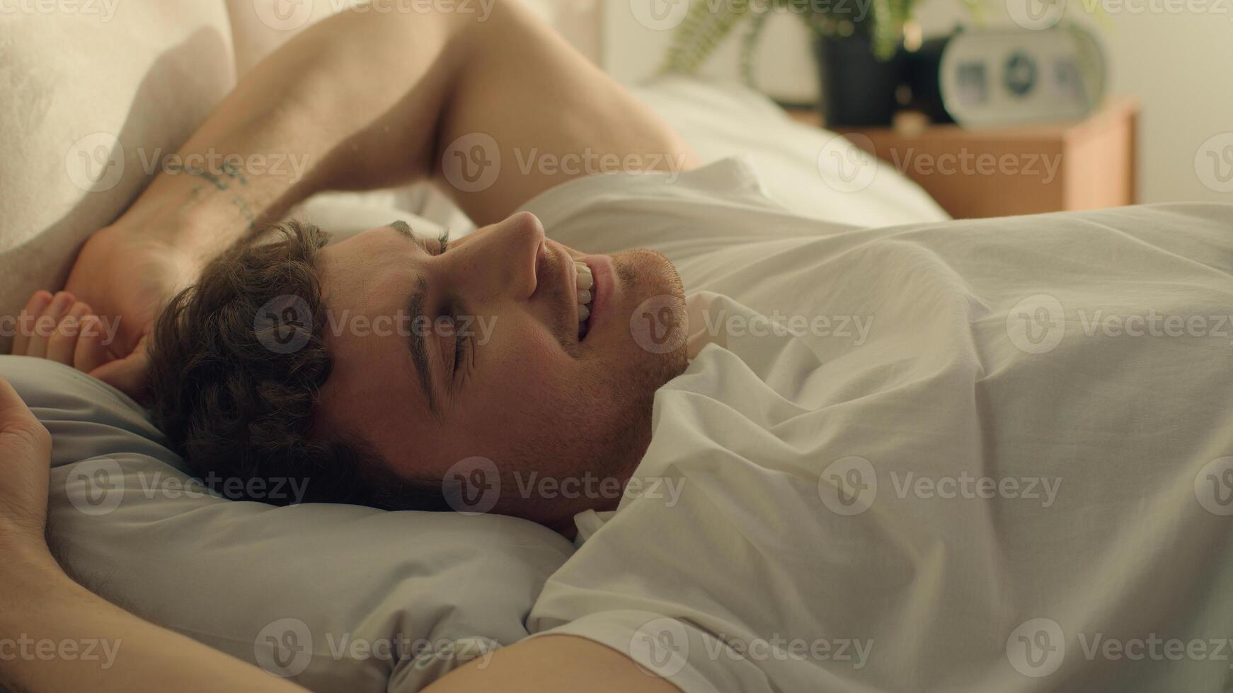 Man wake up lying bed bedroom stretching good morning happy male guy weekend home comfortable smile hotel orthopedic mattress daydream slumber peaceful relaxing positive wellbeing cozy napping dreamy photo
