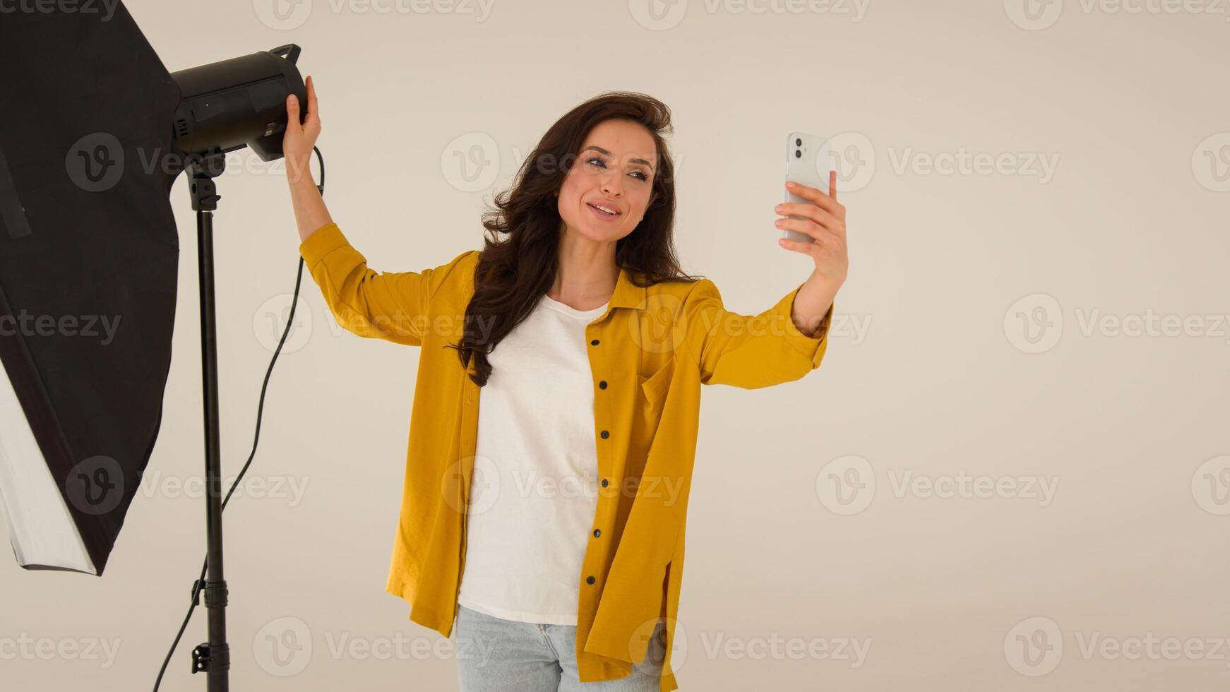 Smiling cheerful Caucasian woman female influencer blogger shooting blog wave hello mobile phone smartphone. Girl vlogger talk walk showing studio clothes streaming broadcast live online at home photo