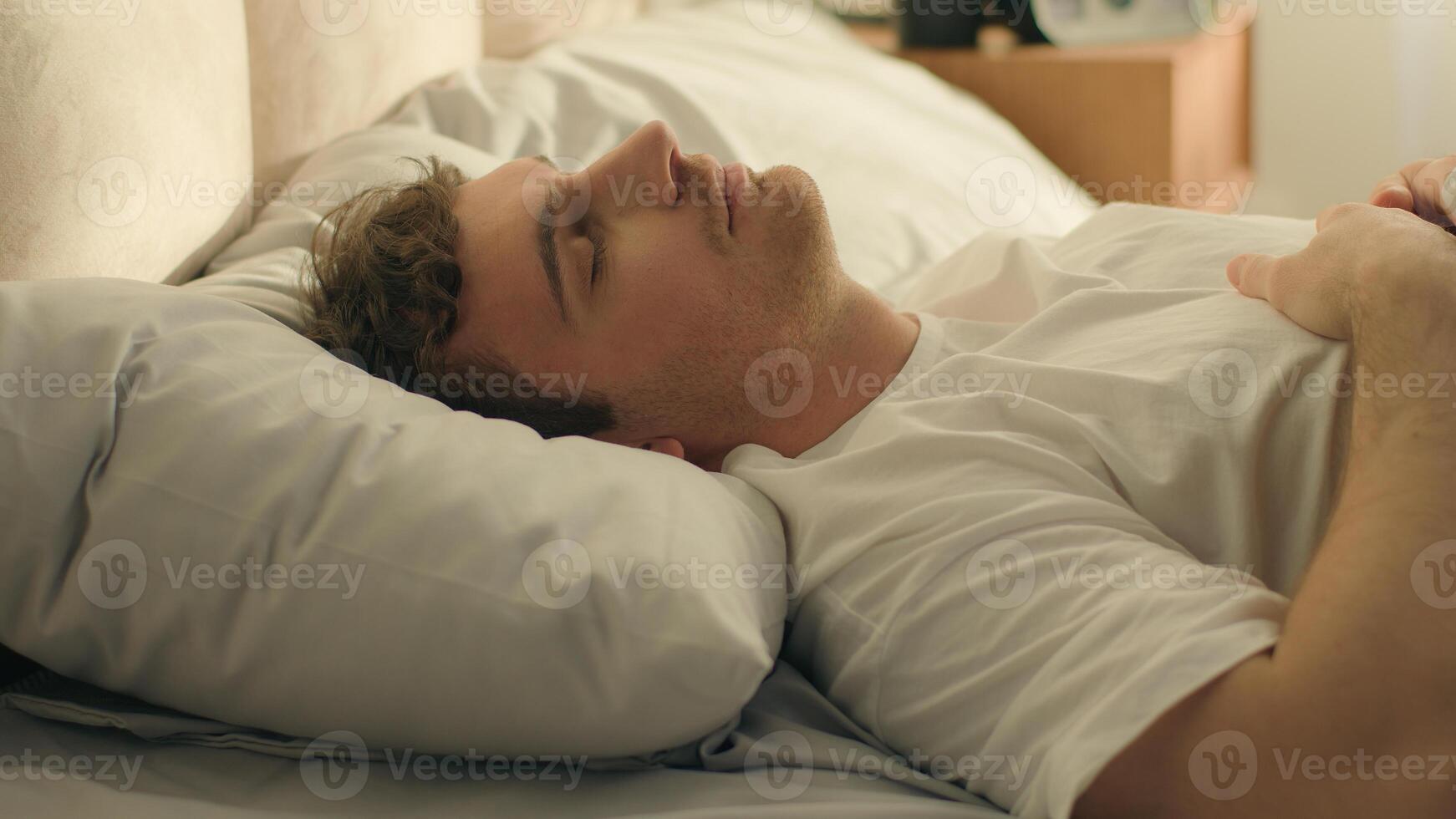 Caucasian man wake up looking mobile phone smartphone telephone gadget sleepy continue sleep lying on bed male weekend check time lazy daydream slumber nap resting technology device guy home bedroom photo