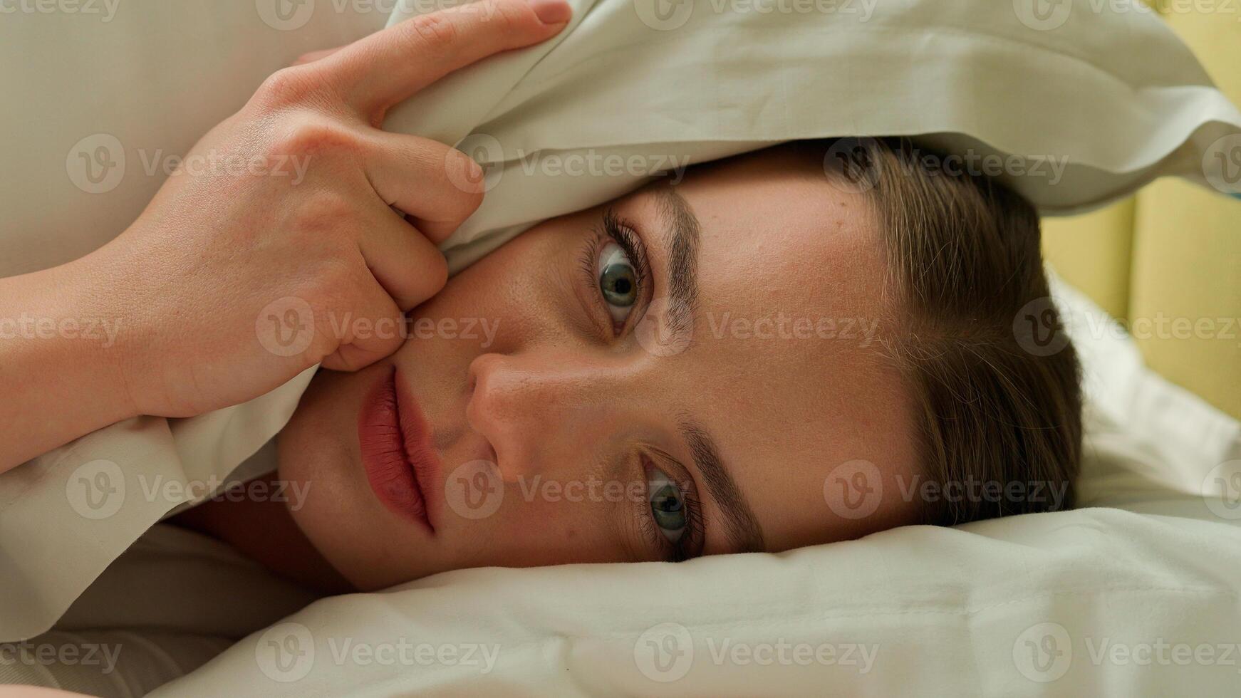 Caucasian stressed sleepy napping tired exhausted fatigued girl dissatisfied sad upset early morning woman awake female at home bedroom wake up cover head with pillow loud alarm clock lying in bed photo