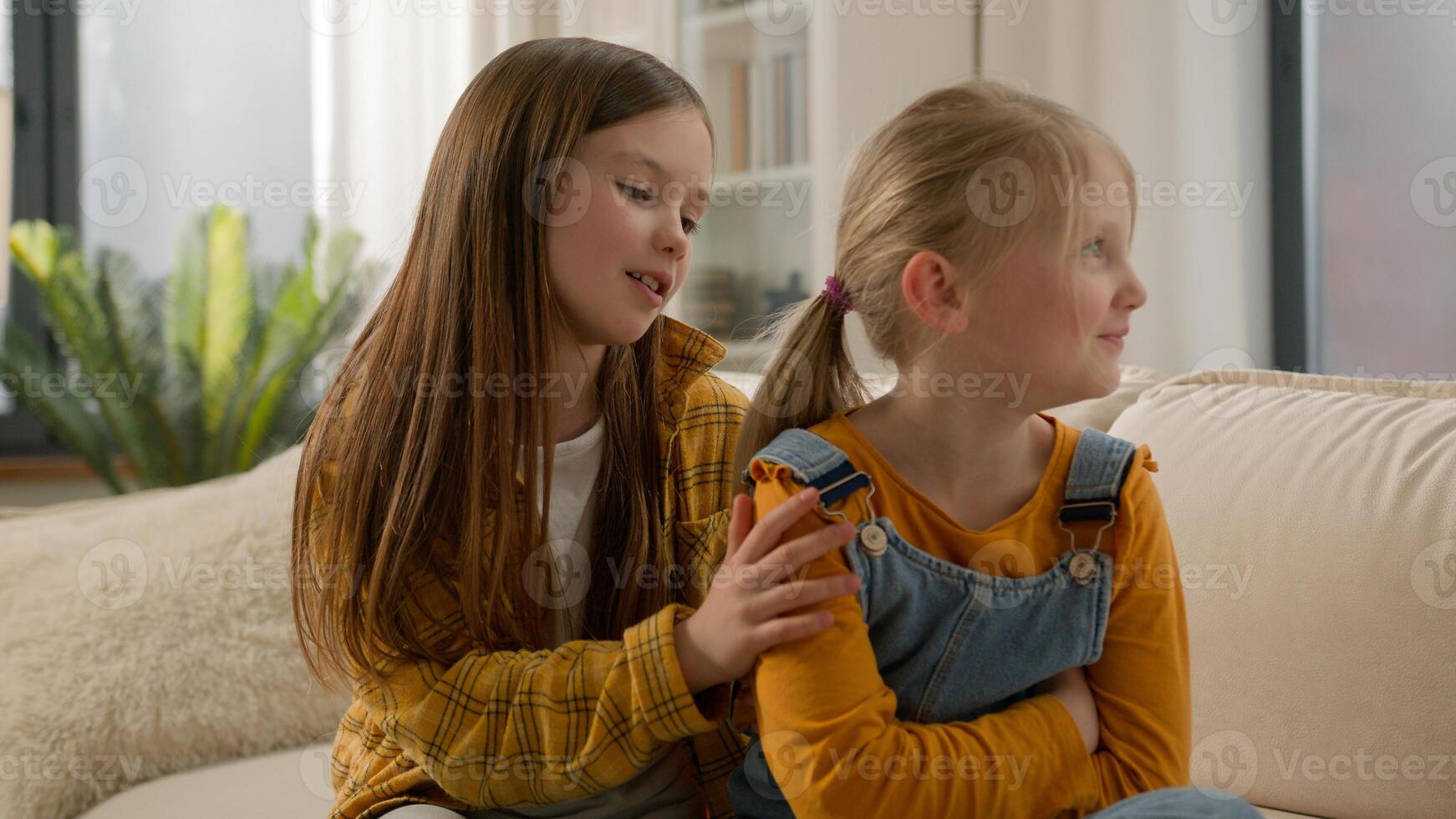 Upset sad little Caucasian children kids argument conflict. Offended girls friends ignoring boycott sisters asking forgiveness apology guilty daughters touch telling sorry sofa home friendship trouble photo