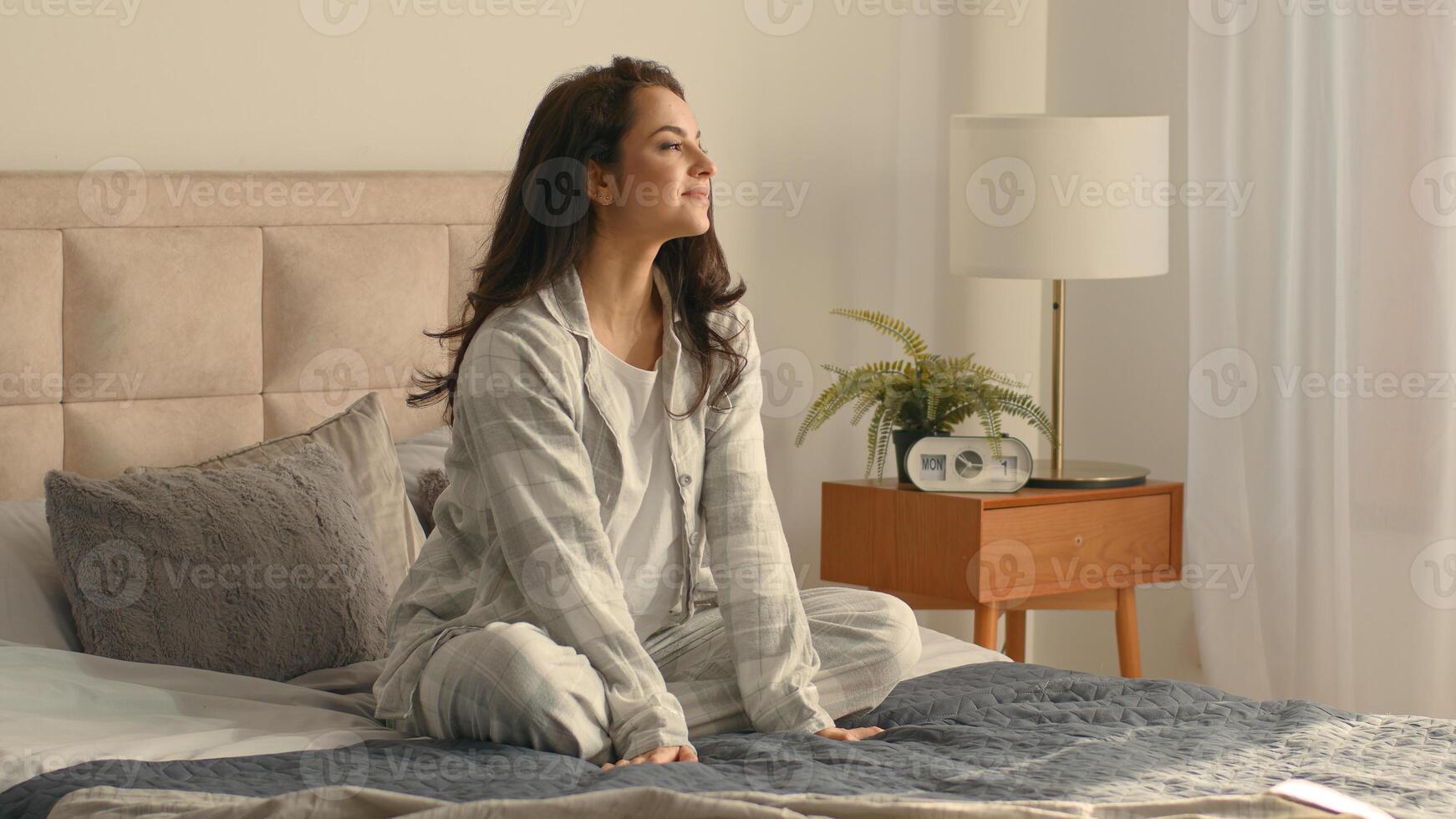 Caucasian brunette woman sitting on bed bedroom home touching neck massage good morning calm comfortable cozy inside awake healthcare in pajamas relaxing smiling wellbeing peaceful apartment recovery photo