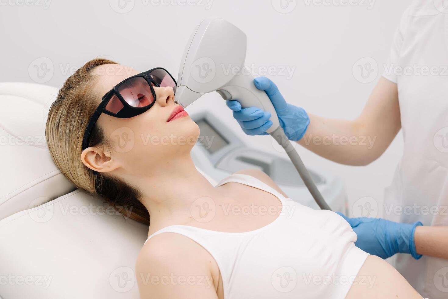 Close-up of a female patient wearing protective glasses during a laser facial hair removal treatment. Advanced depilation technology in a professional aesthetic clinic for smooth, flawless skin photo