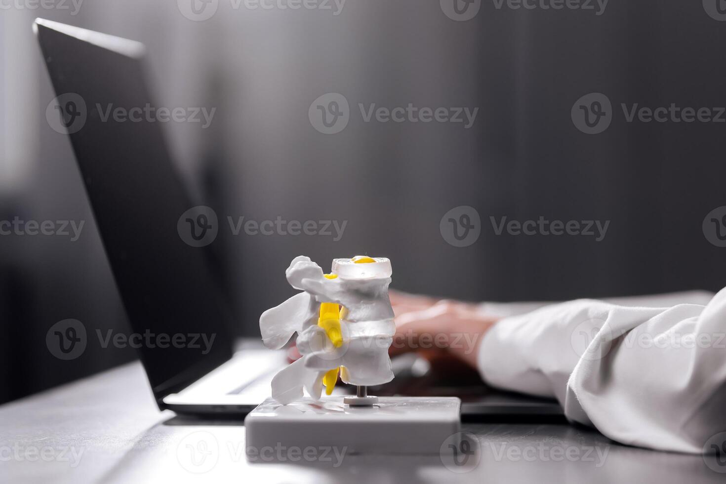 Close-up of a spine model on a physiotherapist's desk, alongside a laptop and glasses. Ideal for depicting spinal treatment procedures and orthopedic care in a modern medical environment photo