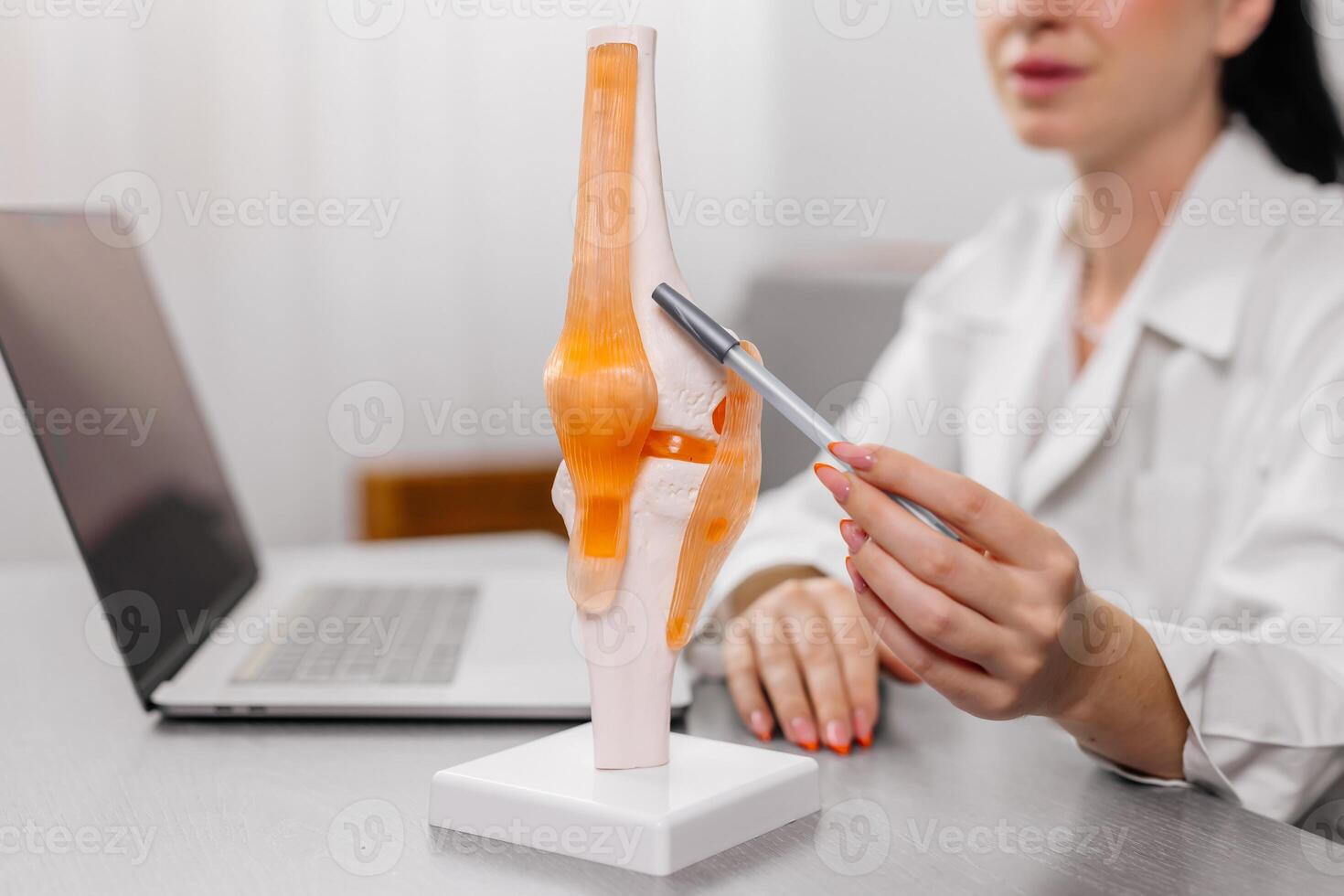 Orthopedic surgeon shows a detailed knee joint model during a medical consultation, demonstrating treatment methods. Ideal for illustrating expert medical advice and advanced orthopedic care photo