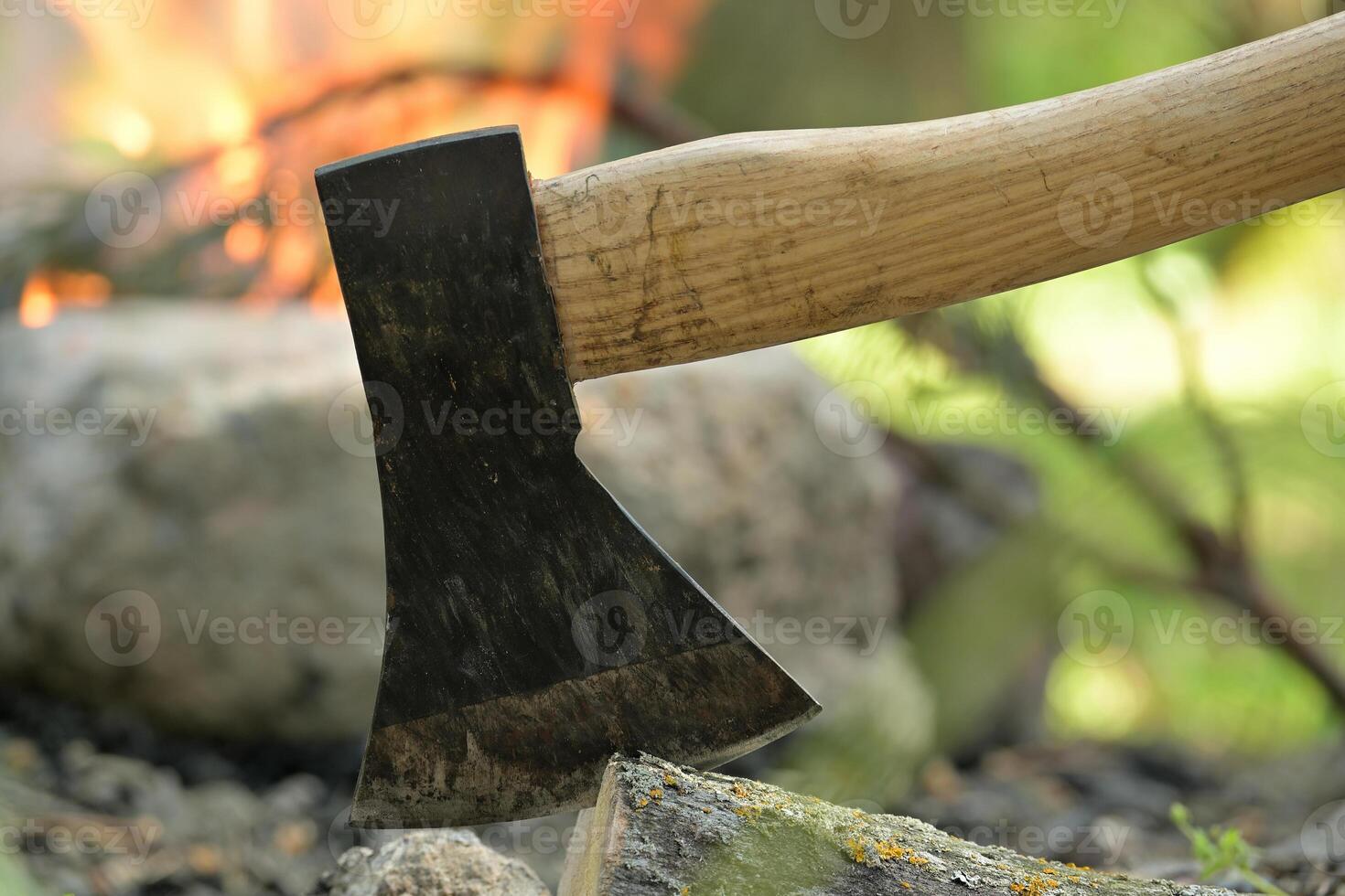 Hatchet lodged in a log of wood, situated opposite a campfire photo