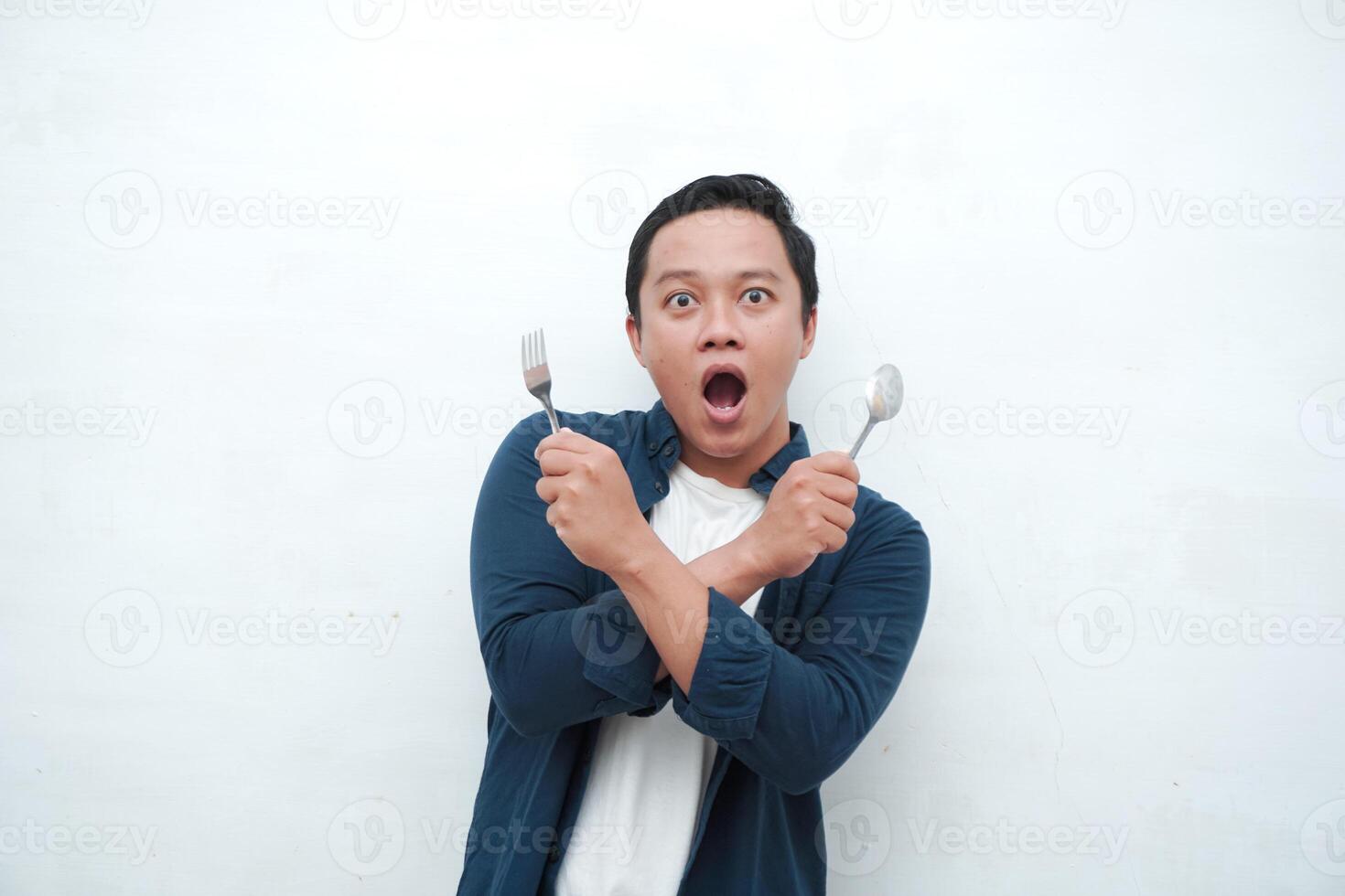 Asian man crossing his arms while holding spoon and fork ready to eat. Diet and healthy eating concept. Avoiding unhealthy food. photo