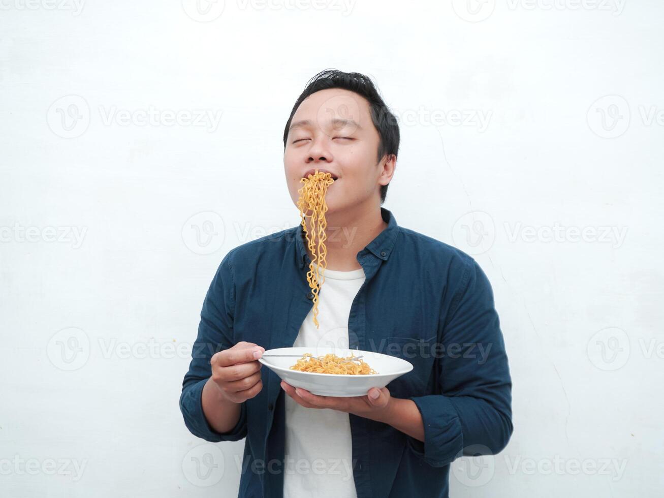 A portrait of happy Asian man wearing a blue shirt excited to eat a plate of fried noodles. Young man smiling and holding a plate of noodle. Isolated with a white background. photo
