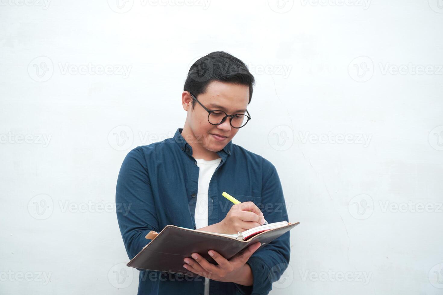 Young Asian man holding a book while thinking and concentrating. Asian student looking for ideas while studying over white background photo
