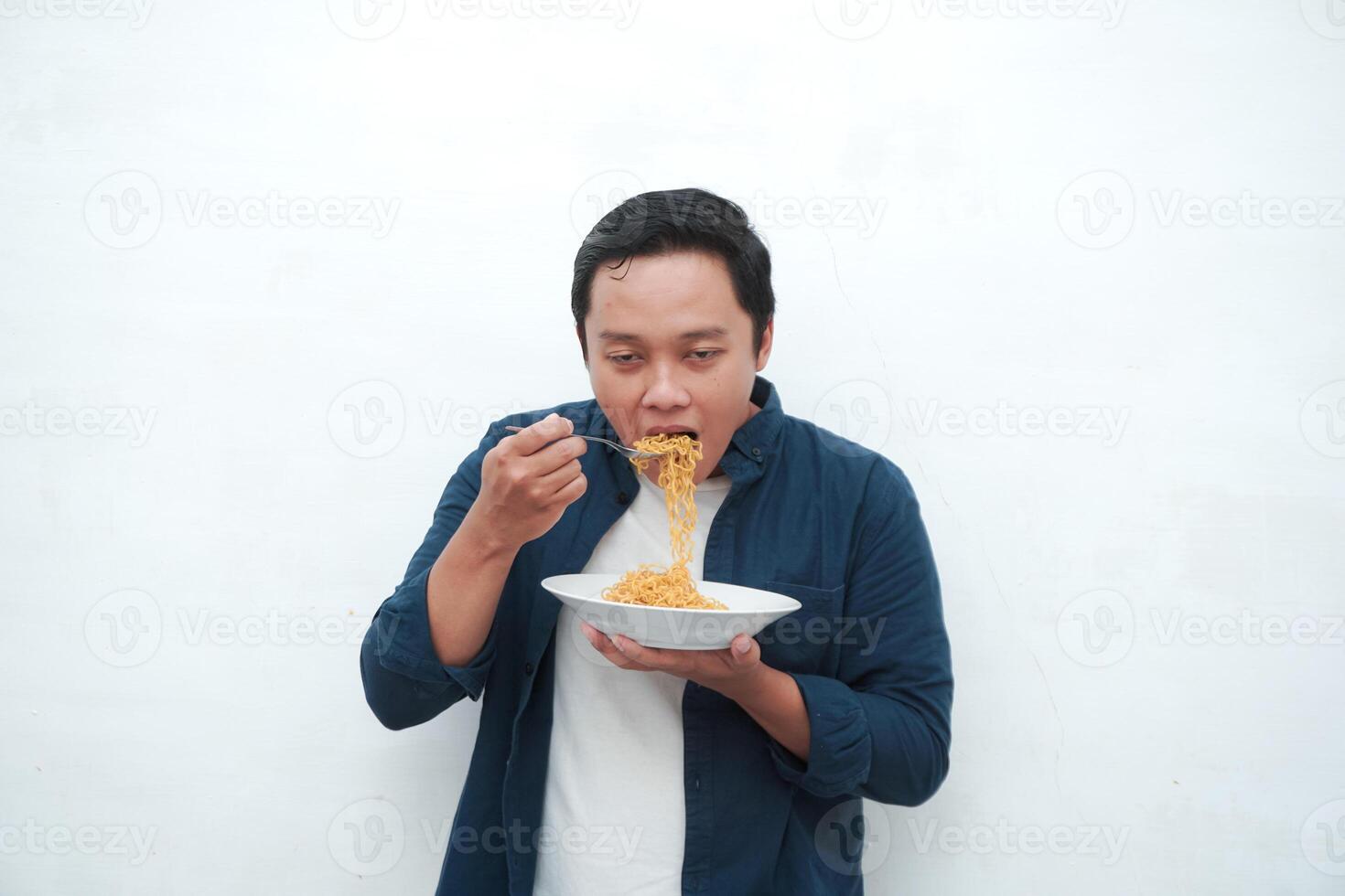 A portrait of happy Asian man wearing a blue shirt excited to eat a plate of fried noodles. Young man smiling and holding a plate of noodle. Isolated with a white background. photo
