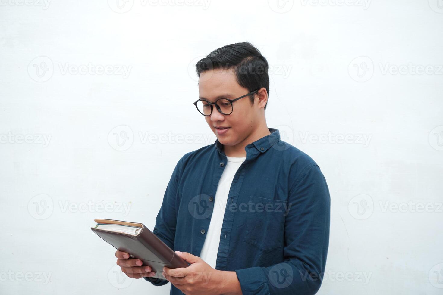 Young Asian man holding a book while thinking and concentrating. Asian student looking for ideas while studying over white background photo