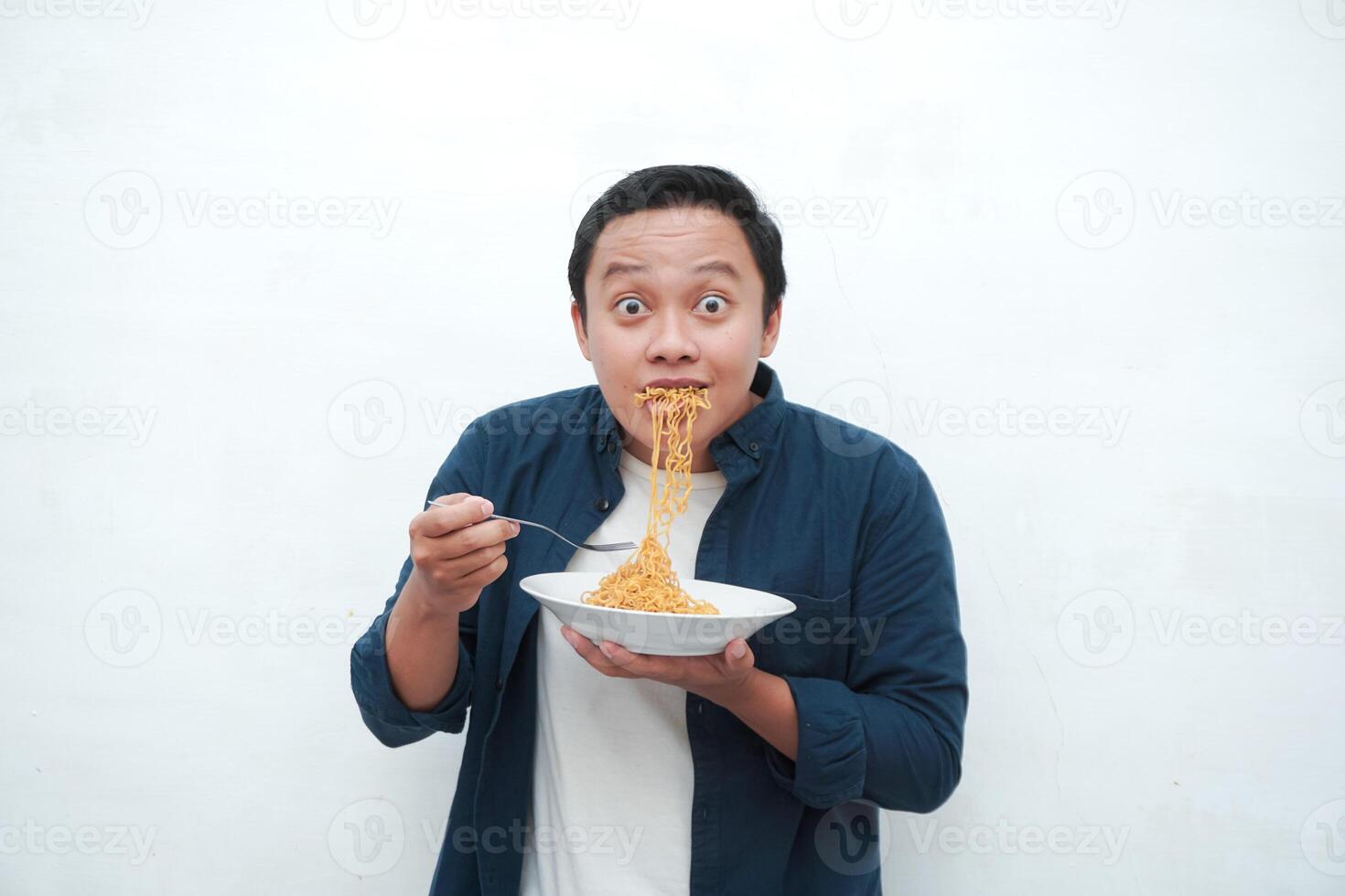 A portrait of happy Asian man wearing a blue shirt excited to eat a plate of fried noodles. Young man smiling and holding a plate of noodle. Isolated with a white background. photo