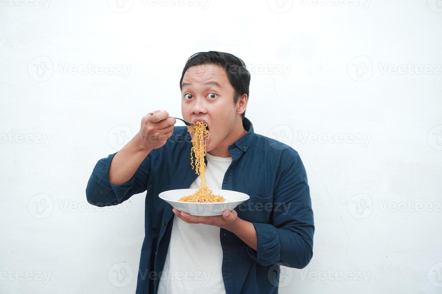 A portrait of happy Asian man wearing a blue shirt excited to eat a plate of fried noodles. Young man smiling and holding a plate of noodle. Isolated with a white background. photo