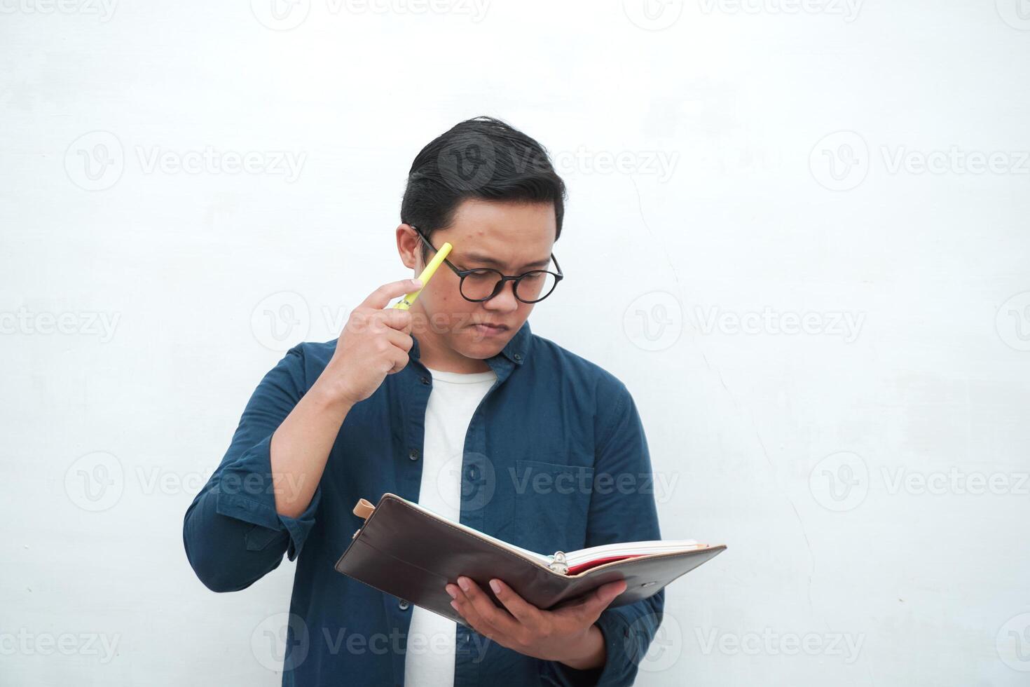 Young Asian man holding a book while thinking and concentrating. Asian student looking for ideas while studying over white background photo