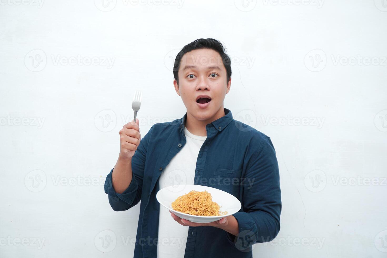 A portrait of happy Asian man wearing a blue shirt excited to eat a plate of fried noodles. Young man smiling and holding a plate of noodle. Isolated with a white background. photo