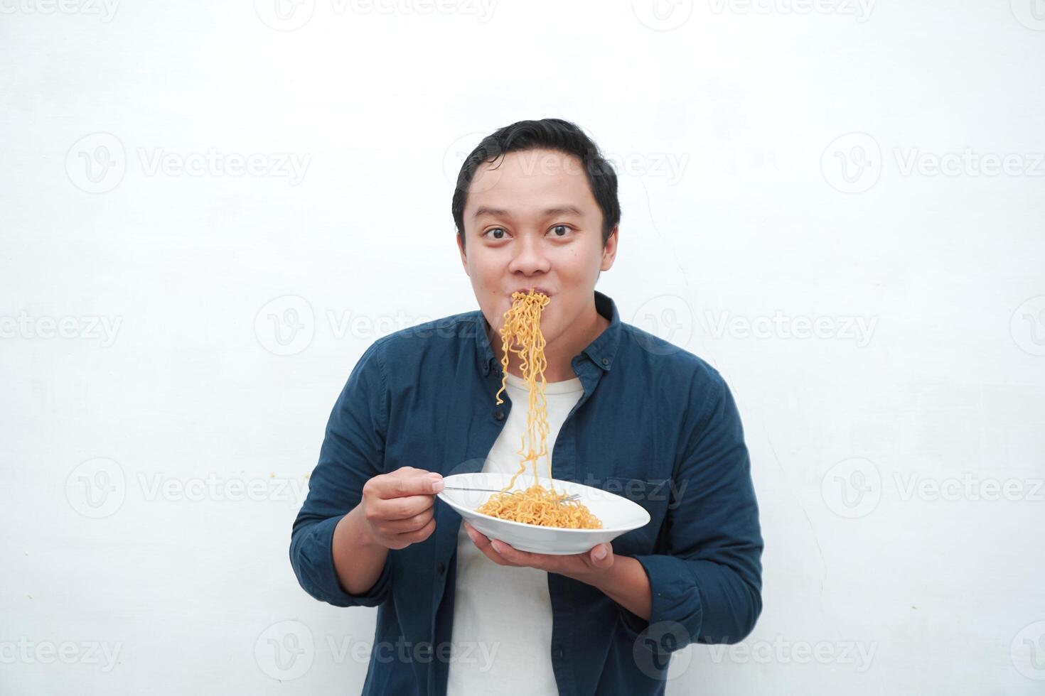 A portrait of happy Asian man wearing a blue shirt excited to eat a plate of fried noodles. Young man smiling and holding a plate of noodle. Isolated with a white background. photo
