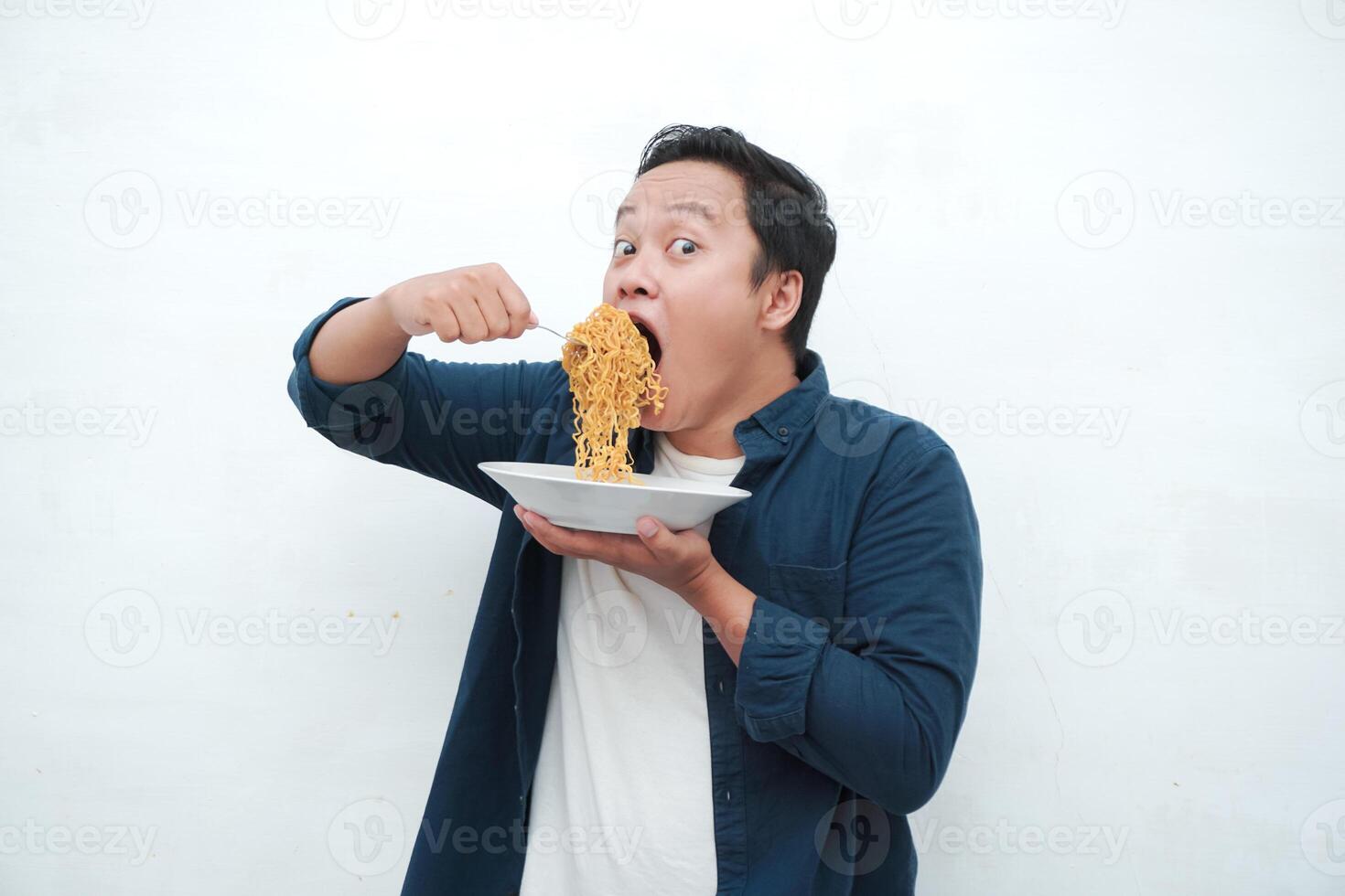 A portrait of happy Asian man wearing a blue shirt excited to eat a plate of fried noodles. Young man smiling and holding a plate of noodle. Isolated with a white background. photo