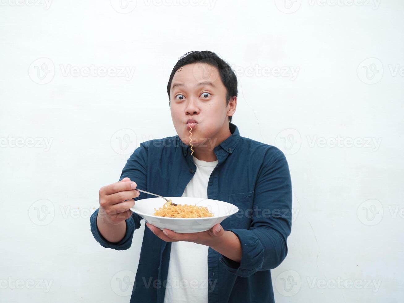 A portrait of happy Asian man wearing a blue shirt while holding a plate of fried noodles. Young man smiling and pointing to a plate of noodle. Isolated with a white background. photo