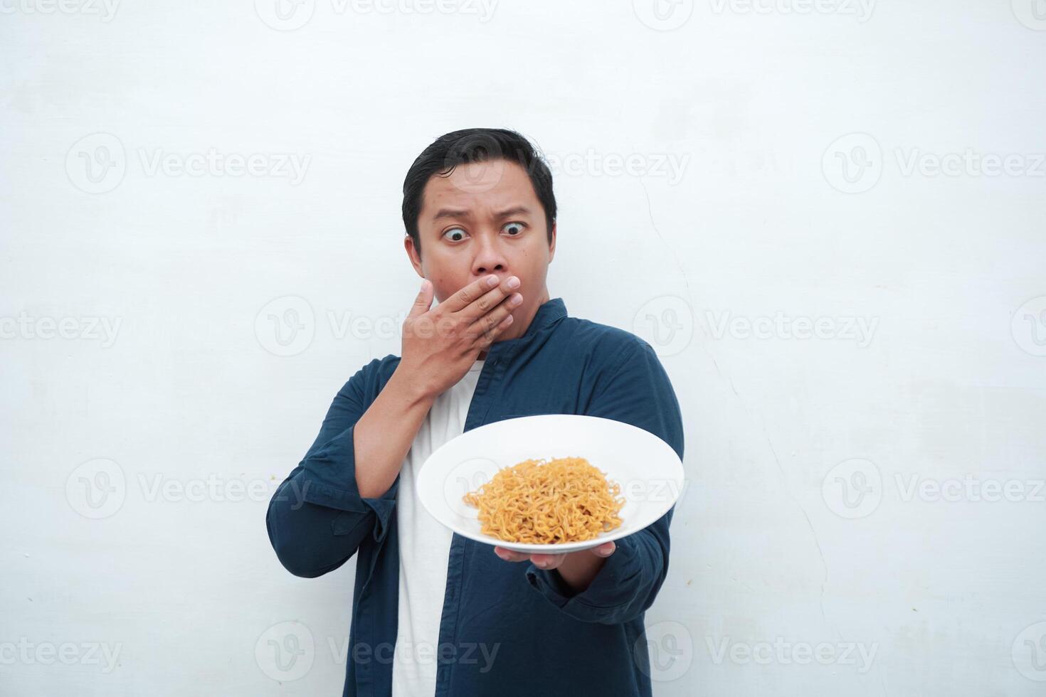 Asian man covering his mouth and nose while holding a plate of fried noodle. Covering mouth and nose because of bad smell of food photo