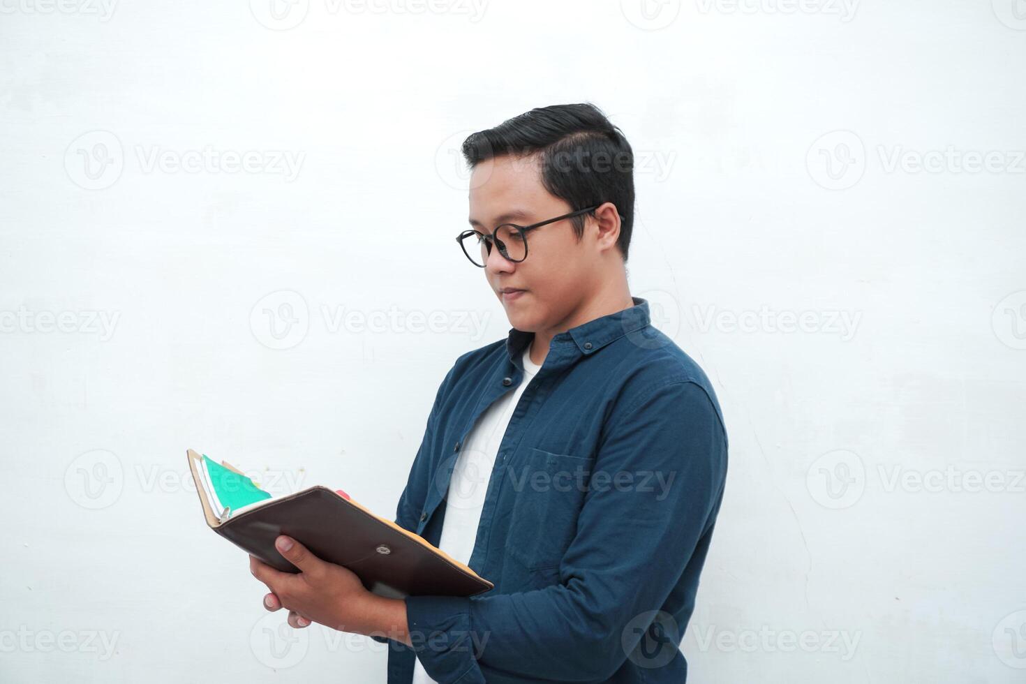 Young Asian man holding a book while thinking and concentrating. Asian student looking for ideas while studying over white background photo