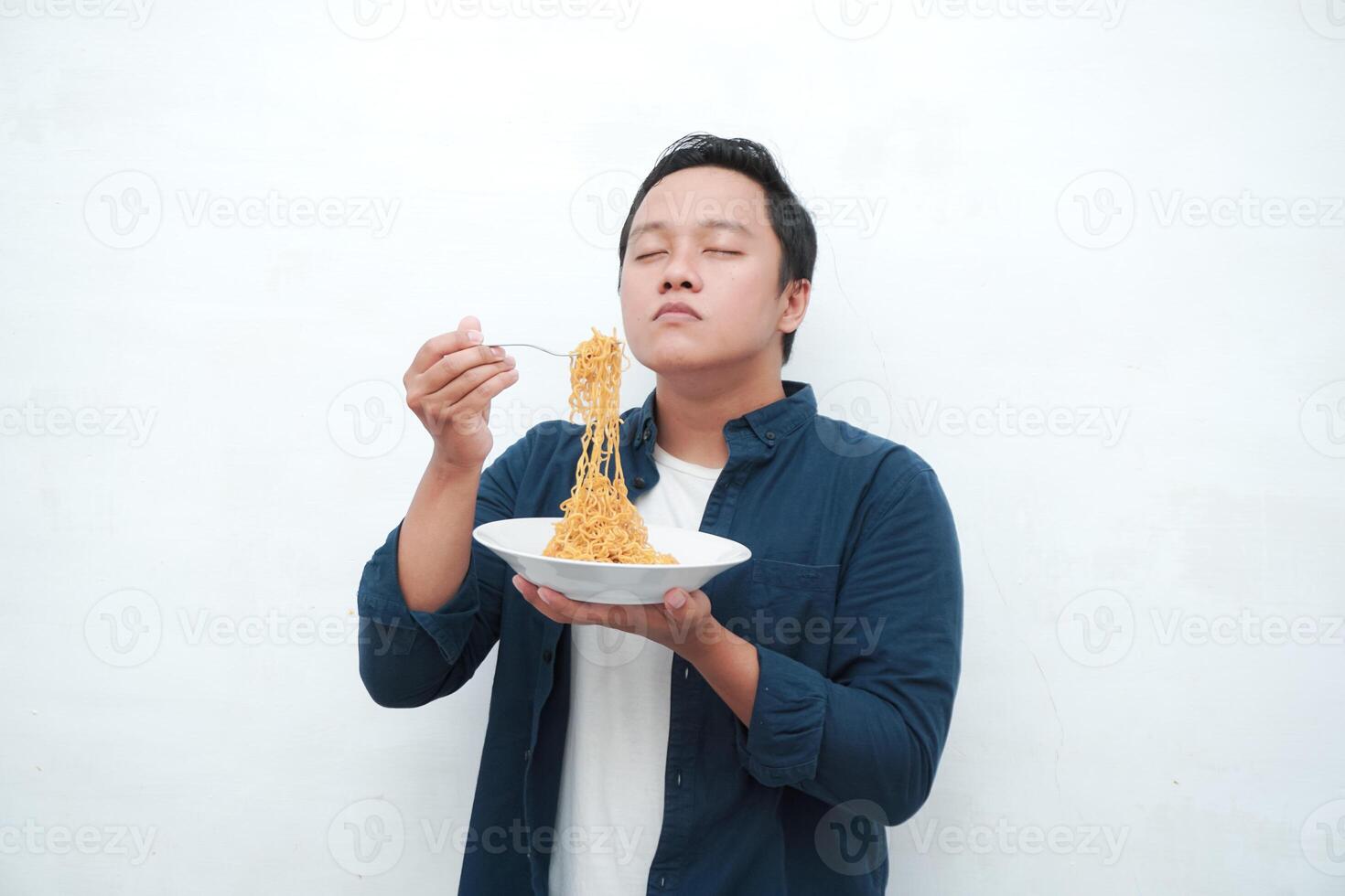 A portrait of happy Asian man wearing a blue shirt excited to eat a plate of fried noodles. Young man smelling the aroma of delicious fried noodles. Isolated with a white background. photo