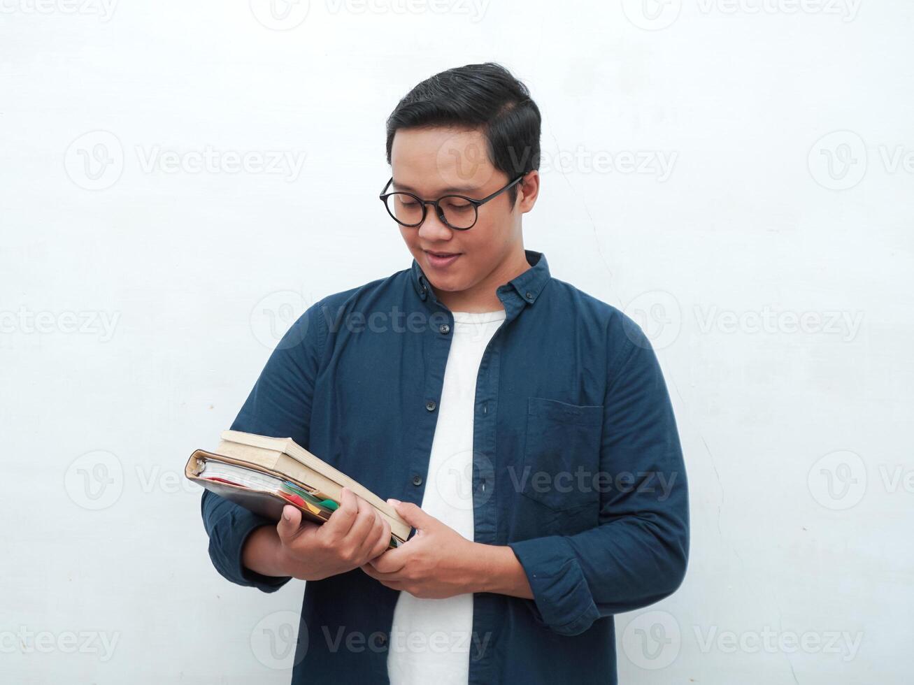 Young Asian man holding books smiling happy and positive while reading a book. Asian student flipping a book page over white background photo