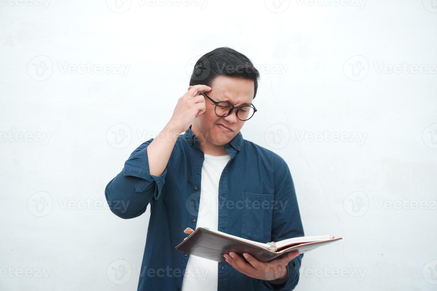 Young Asian man holding a book while thinking and concentrating. Asian student looking for ideas while studying over white background photo