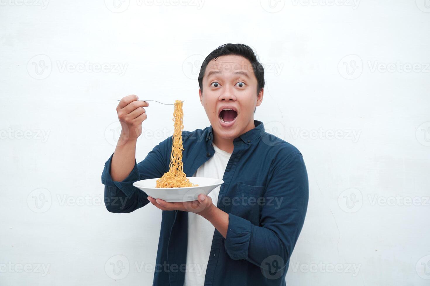 A portrait of happy Asian man wearing a blue shirt excited to eat a plate of fried noodles. Young man smiling and holding a plate of noodle. Isolated with a white background. photo