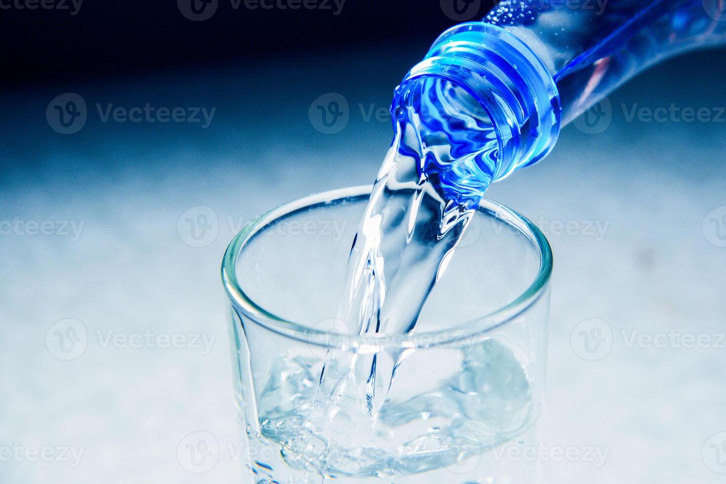 Close-Up of Water Being Poured from a Blue Plastic Bottle into a Glass on a Light Background photo