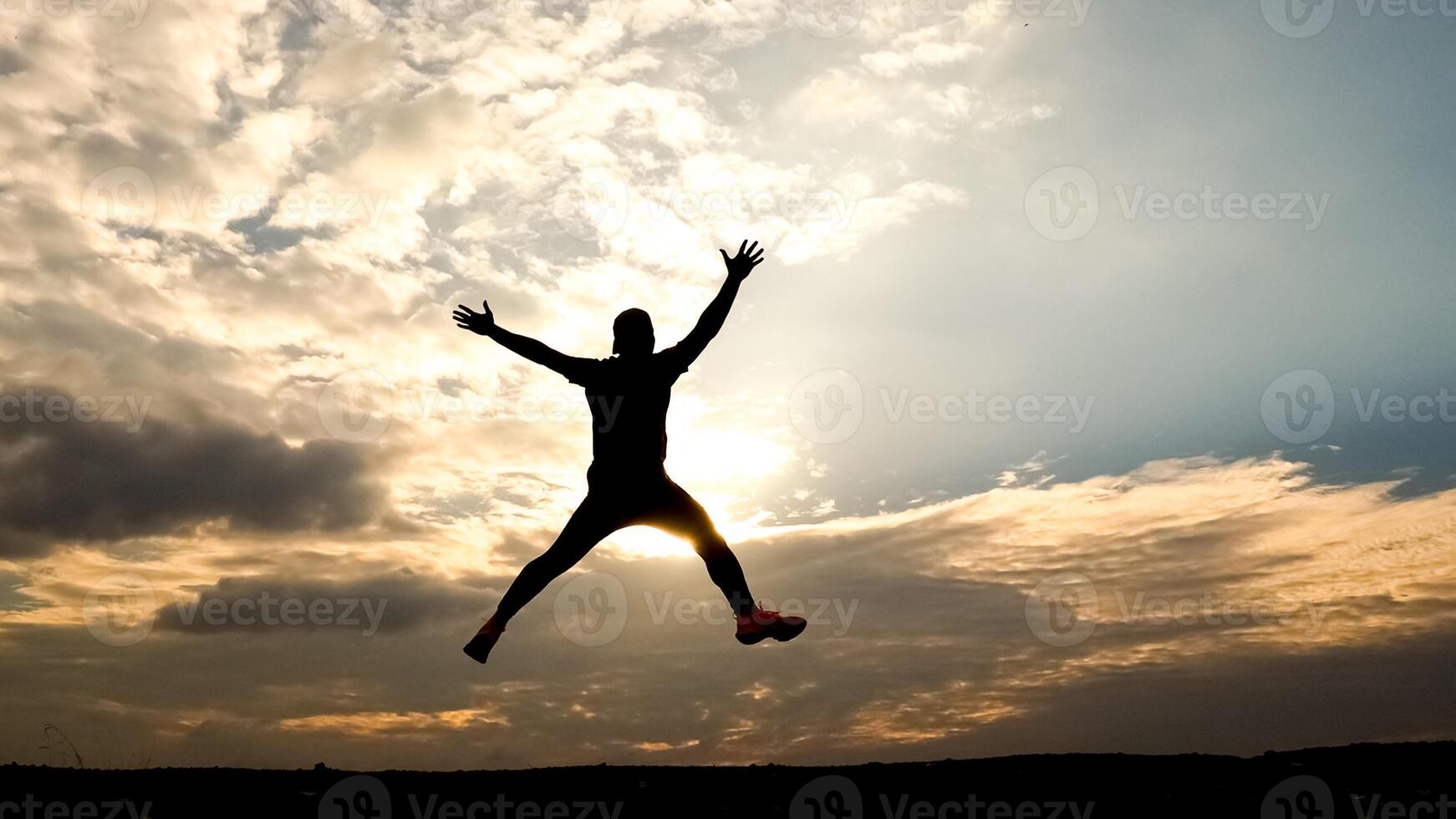 Silhouette of a Person Jumping Against a Dramatic Sunset Sky with Clouds in the Background photo