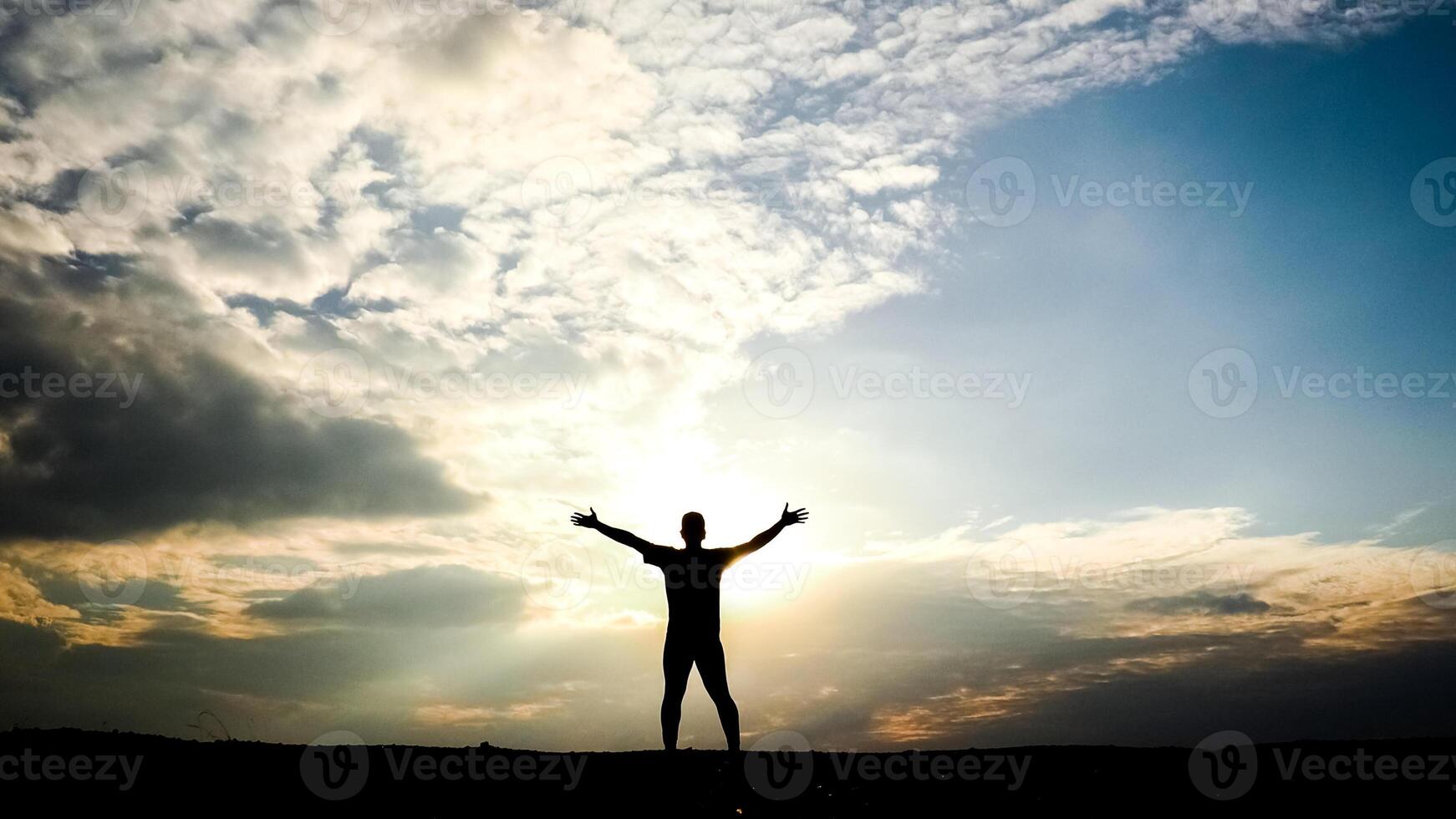 Silhouette of a Person with Outstretched Arms Against a Dramatic Sunset Sky with Clouds photo