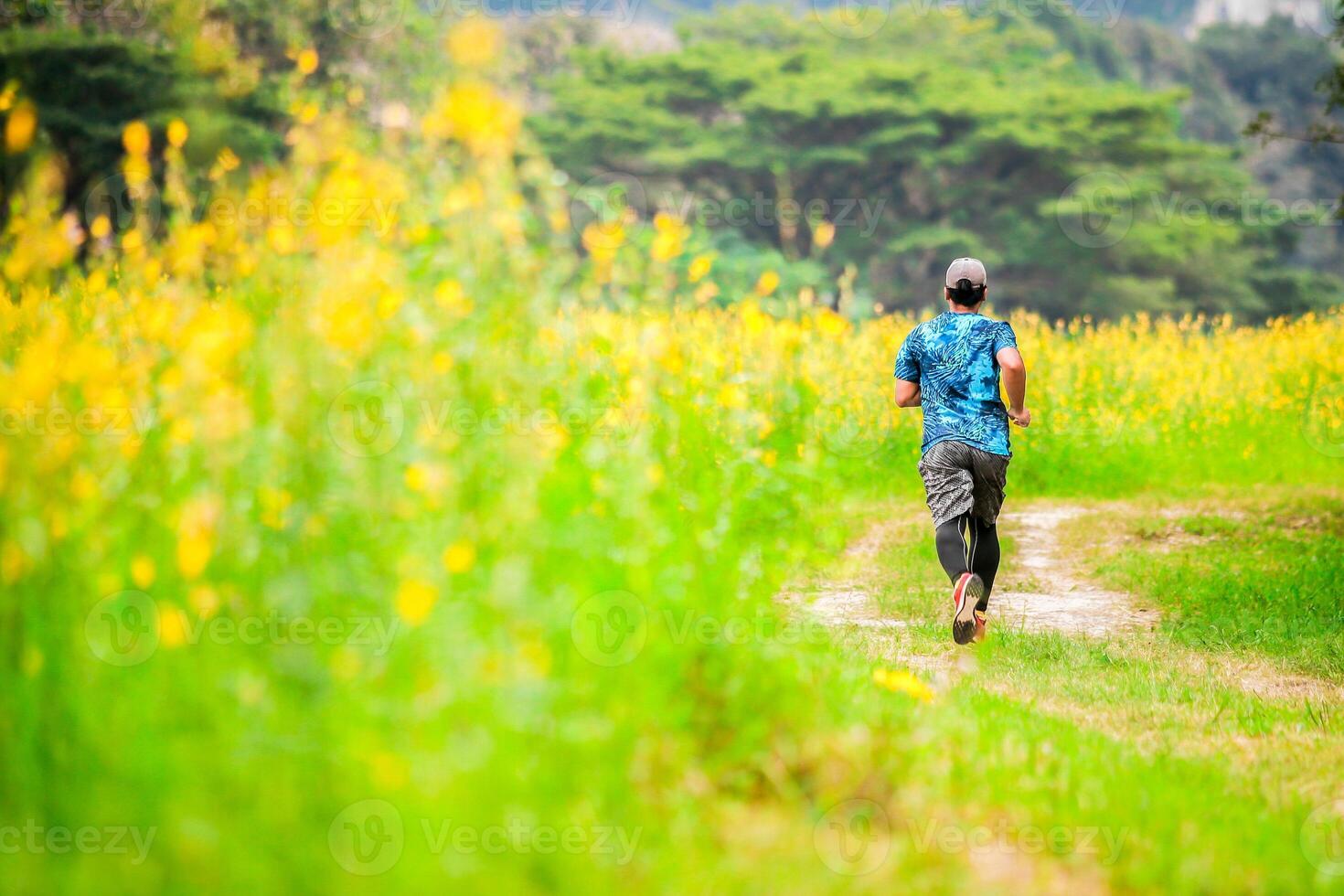 Man Running on a Trail Through a Vibrant Flower Field with Lush Greenery and Trees in the Background photo