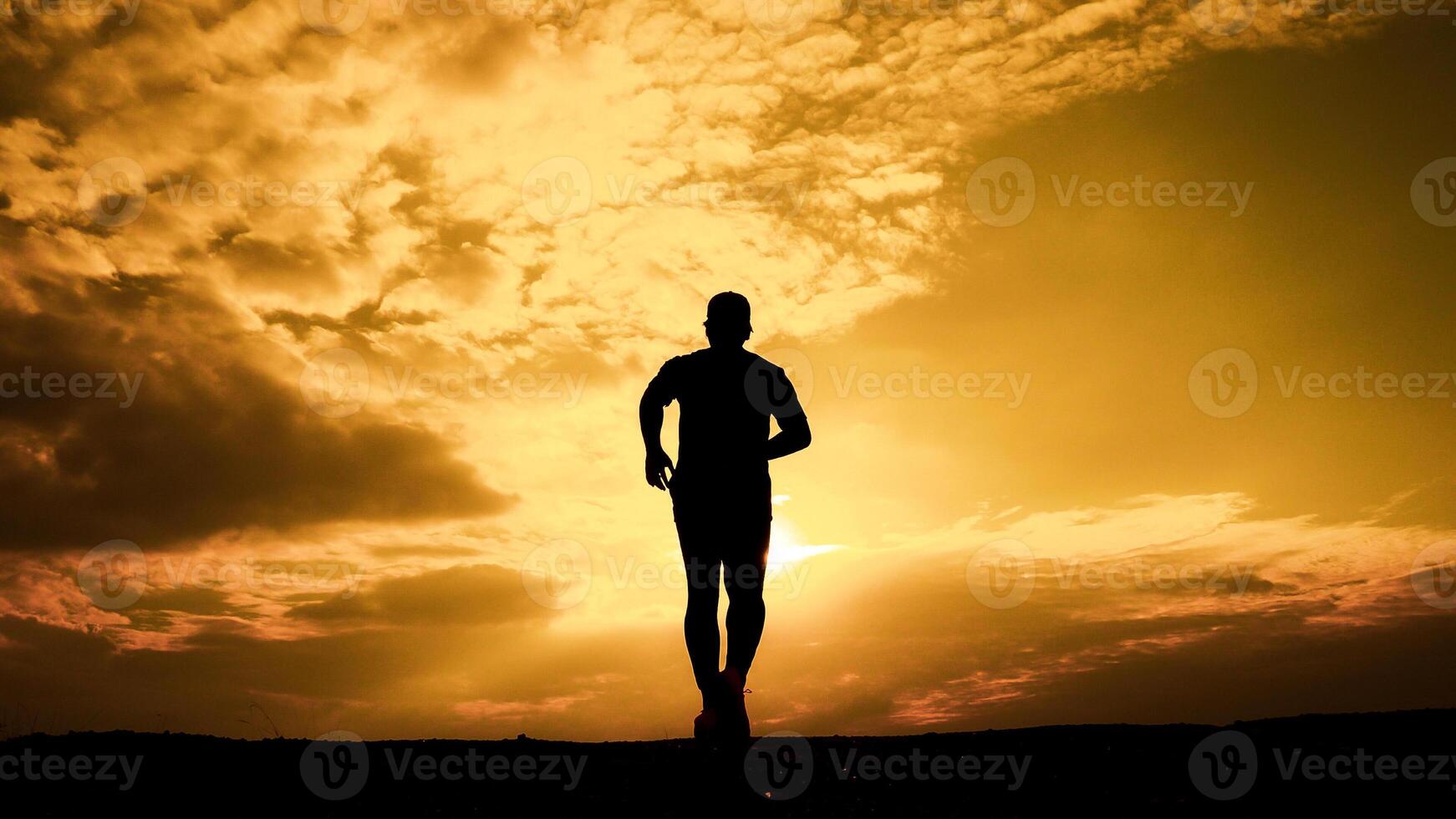Silhouette of a Man Running at Sunset with Dramatic Sky and Golden Clouds in the Background photo