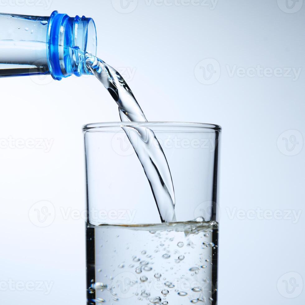 Fresh Water Pouring from Bottle into Glass on White Background with Bubbles and Splash photo
