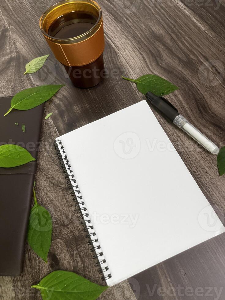 Still life photography blank notebook on wooden table with a cup of coffee, plant, leaf on table photo