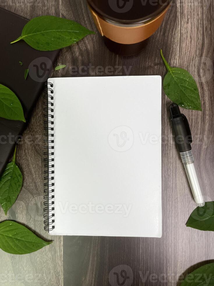 Still life photography blank notebook on wooden table with a cup of coffee, plant, leaf on table photo