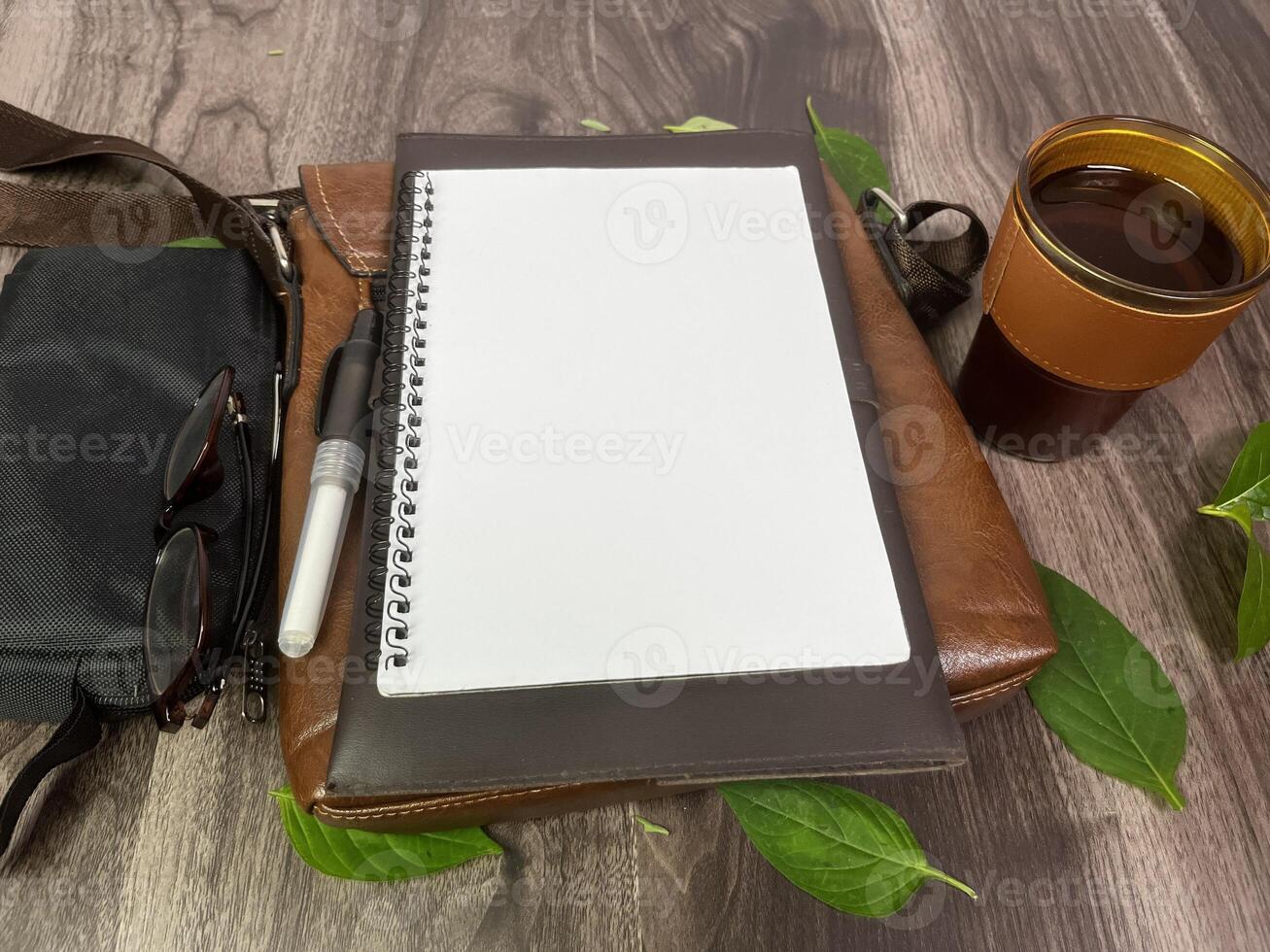 Still life photography blank notebook on wooden table with a cup of coffee, plant, leaf on table photo