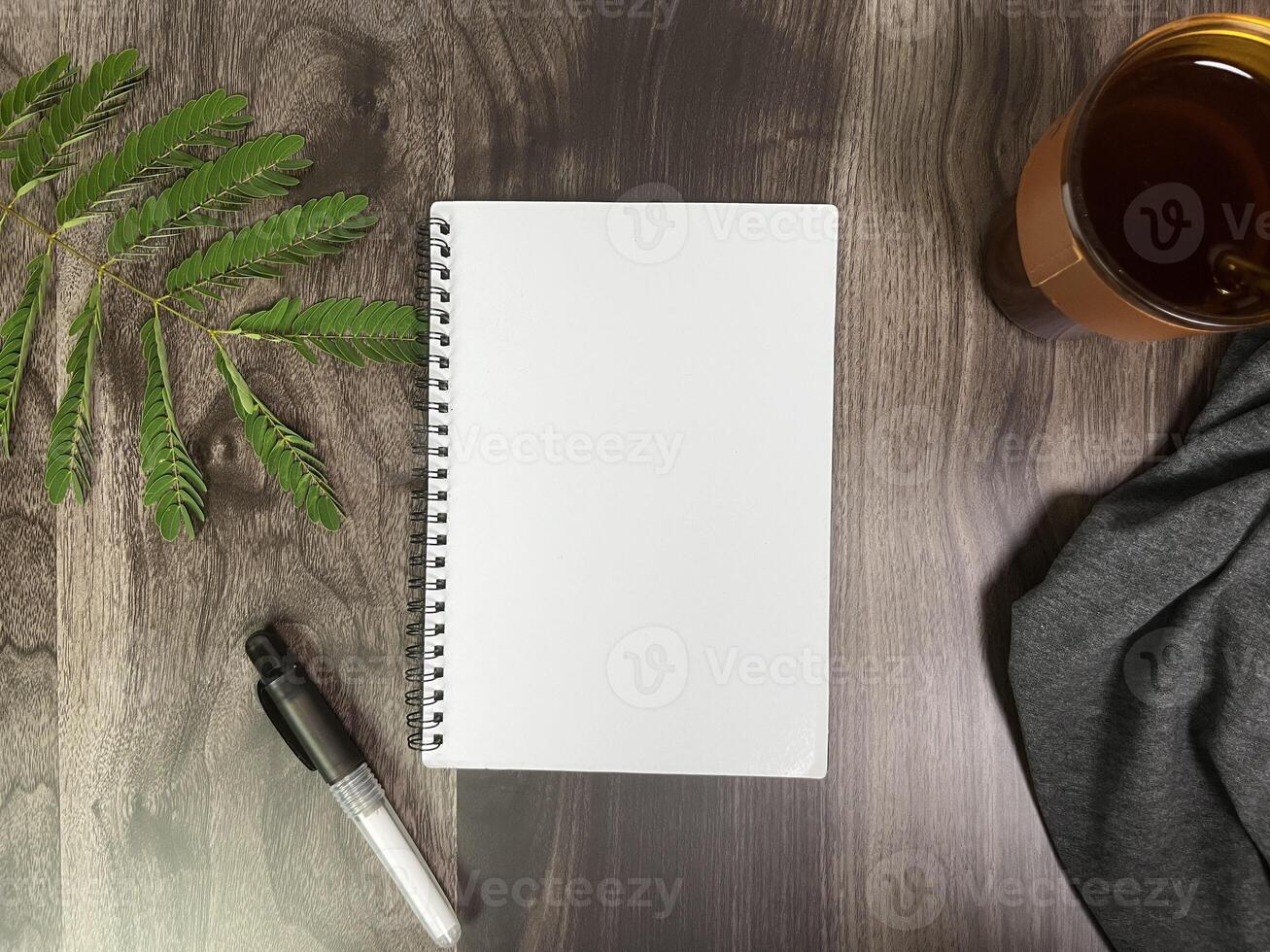 Still life photography blank notebook on wooden table with a cup of coffee, plant, leaf on table photo