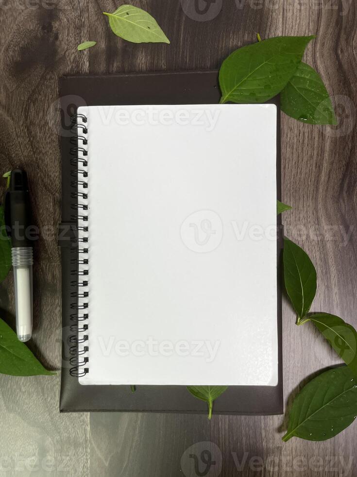 Still life photography blank notebook on wooden table with a cup of coffee, plant, leaf on table photo