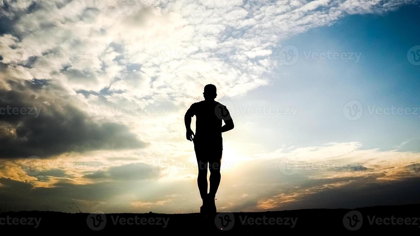 Silhouette of a Man Running at Sunset with Dramatic Sky and Clouds in the Background photo