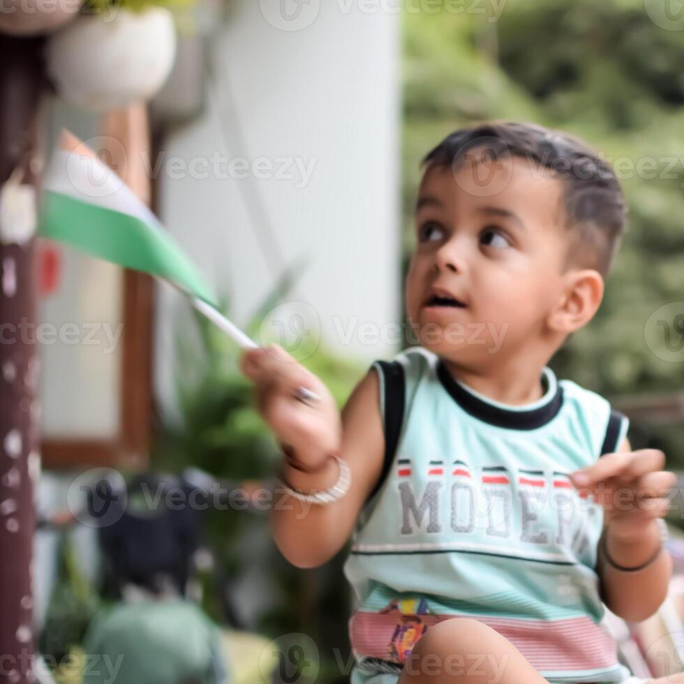 Cute Indian boy holding Indian National Flag in his hangs at home balcony. Bright portrait of happy child sitting on the table with national flag photo