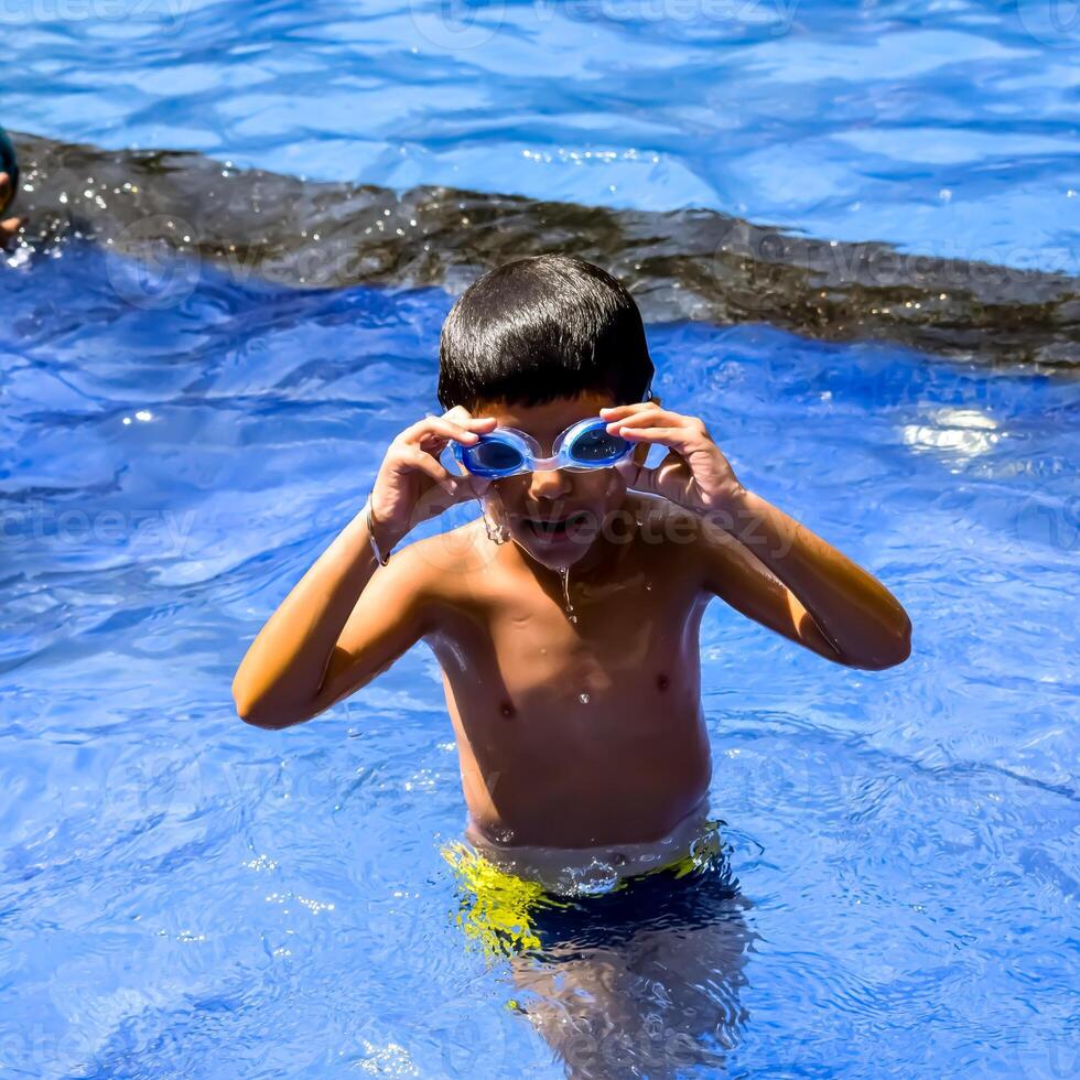 Happy Indian boy swimming in a pool, Kid wearing swimming costume along with air tube during hot summer vacations, Children boy in big swimming pool. photo