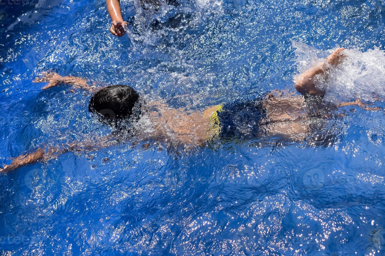 Happy Indian boy swimming in a pool, Kid wearing swimming costume along with air tube during hot summer vacations, Children boy in big swimming pool. photo