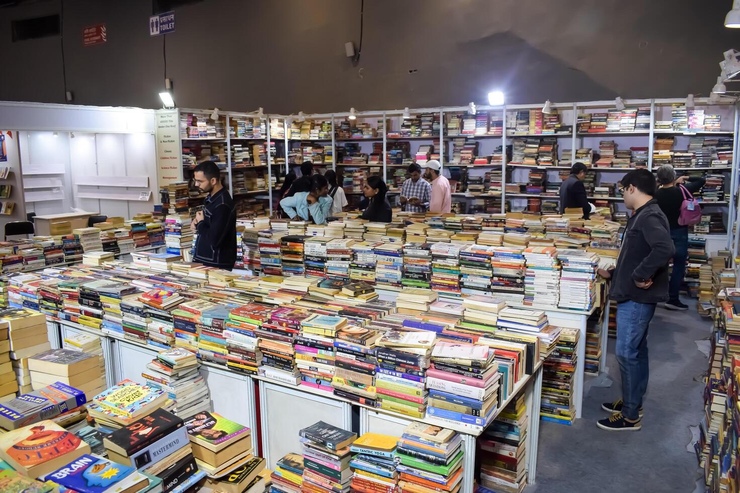 Delhi, India, July 17 2024 - Various age group people reading variety of Books on shelf inside a book-stall at Delhi International Book Fair, Books in Annual Book Fair at Bharat Mandapam complex photo