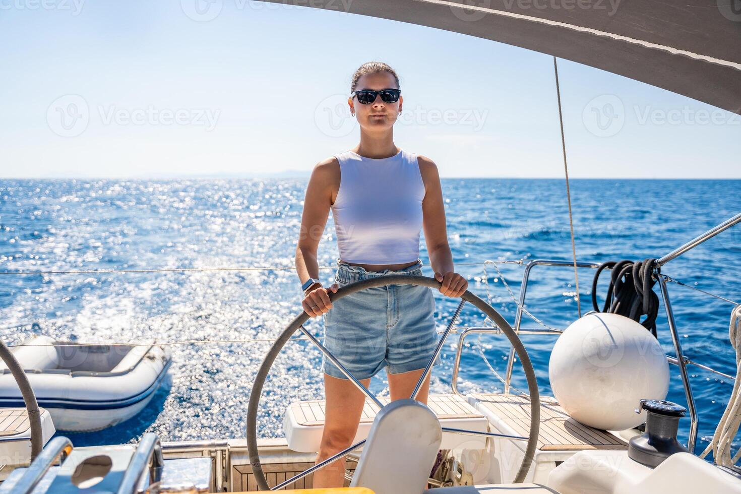 Young woman female captain stands at the helm and controls a sailboat during a journey by sea. High quality photo