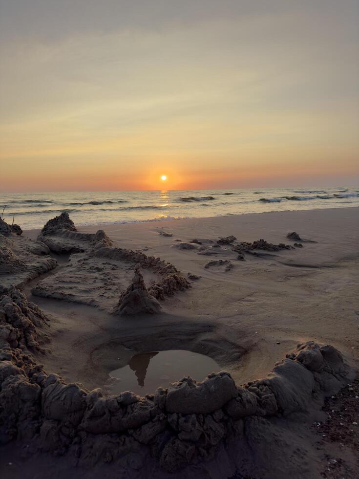 A sand fortress stands proudly on the beach, bathed in the warm glow of the sunset. The soft light highlights the intricate details of the structure, casting long shadows on the wet sand as the waves photo