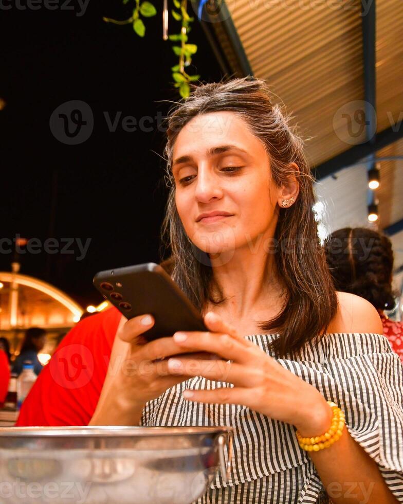 Close up young caucasian woman hold smartphone taking photo of her dinner soup meal from top in public busy restaurant. Social media food content creator concept. Girl using phone at the table