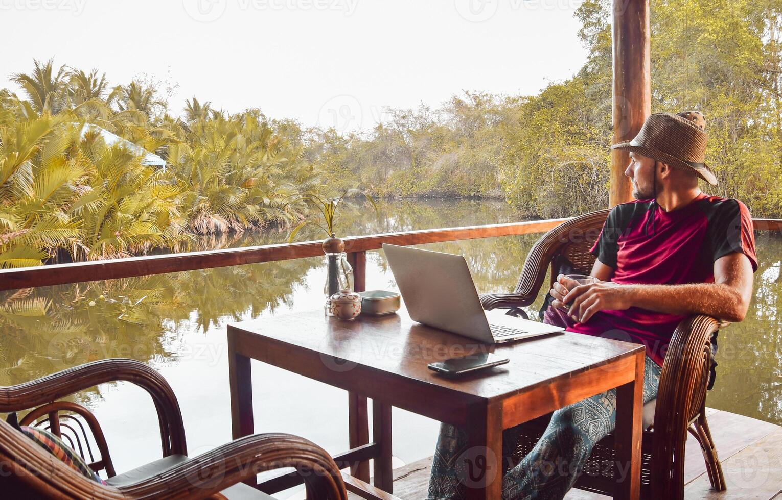 Close up thoughtful young caucasian man tourist sit by table in cafe use laptop on holidays in southeast asia in beautiful tropical nature. Remote worker work online abroad concept photo